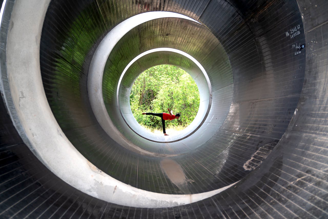 why-choose-us A person is performing a yoga pose inside a large circular metal tunnel with trees visible in the background.